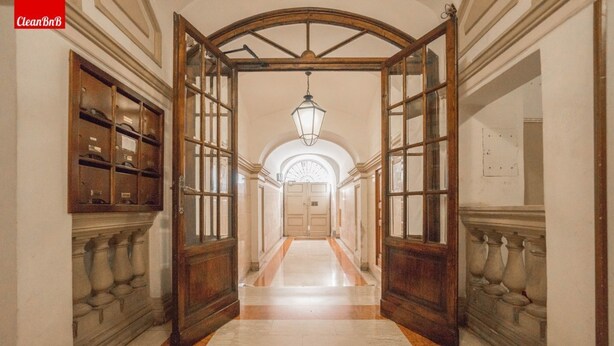 Un pasillo con puerta de madera, lámpara colgante y piso de mármol.