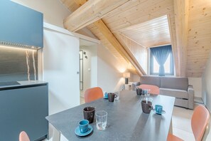 A modern kitchen with a built-in stove, a dining table with chairs, and a high ceiling with exposed wooden beams.