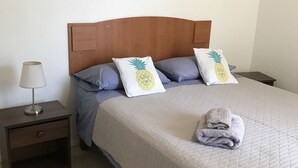 A bedroom with a wooden headboard, a bed with a quilted bedspread, two pillows with pineapple designs, a nightstand with a lamp, and two paintings on the wall. - Amplio y Cómodo Departamento Full Amoblado a Pasos de Chinchorro , Mall (Arica)