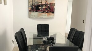A conference room with a glass table, four black chairs, and a cityscape painting on the wall. - Amplio y Cómodo Departamento Full Amoblado a Pasos de Chinchorro , Mall (Arica)