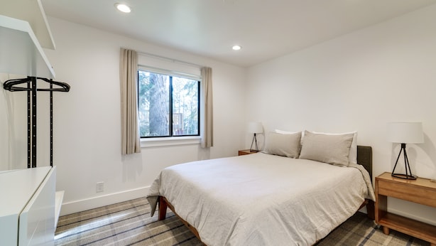 A bedroom with a bed, bedside tables, a lamp, a window with curtains, and a hanging light fixture. - Steps to Beach: Family Home w/ Views in Tahoe City (Tahoe City)