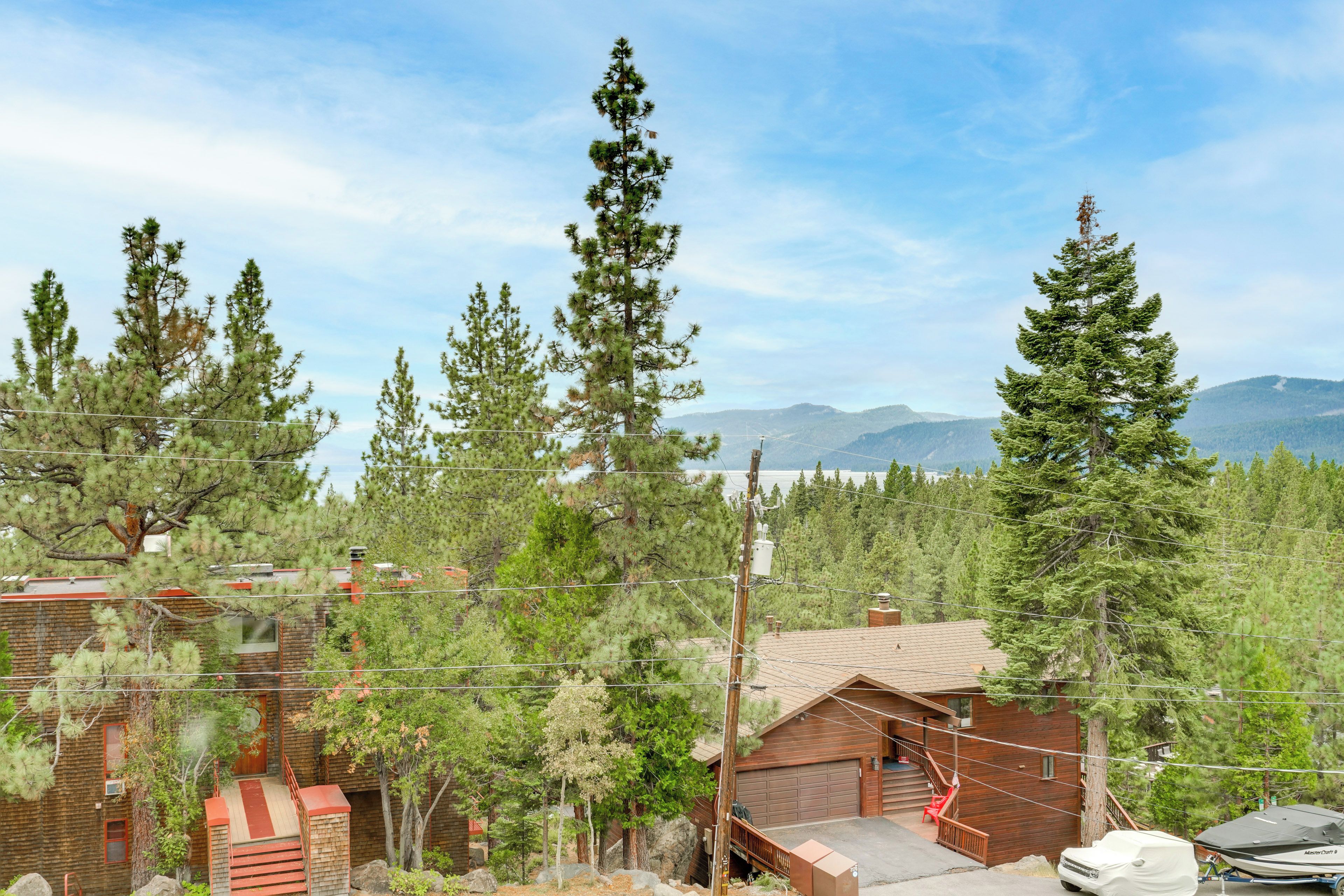 A cabin with a garage, surrounded by tall pine trees, with a mountain range in the background.