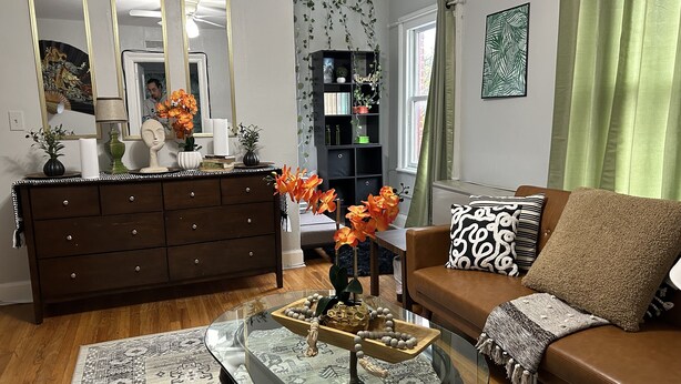 A living room with a brown sofa, a glass coffee table, a dark wooden dresser, and a green plant. - Chic Madison Parkview
 (Albany)