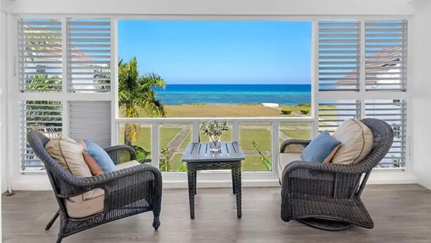 A room with wicker chairs, a small table, and a large window overlooking a beach. - Modern Apartment Montego Bay in Jamaica (Montego Bay)
