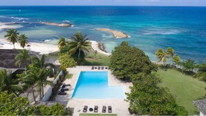 A resort with a swimming pool, palm trees, and a view of the ocean. - Modern Apartment Montego Bay in Jamaica (Montego Bay)