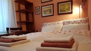 A neatly made bed with folded towels, a wooden chair, and framed pictures on the wall.
