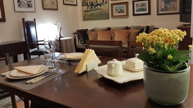 A dining area with a table set for four, a vase of yellow flowers, and framed pictures on the wall.