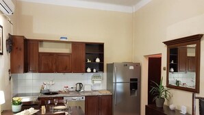 A compact kitchen with wooden cabinets, a stainless steel refrigerator, a dining table with chairs, and a small potted plant.
