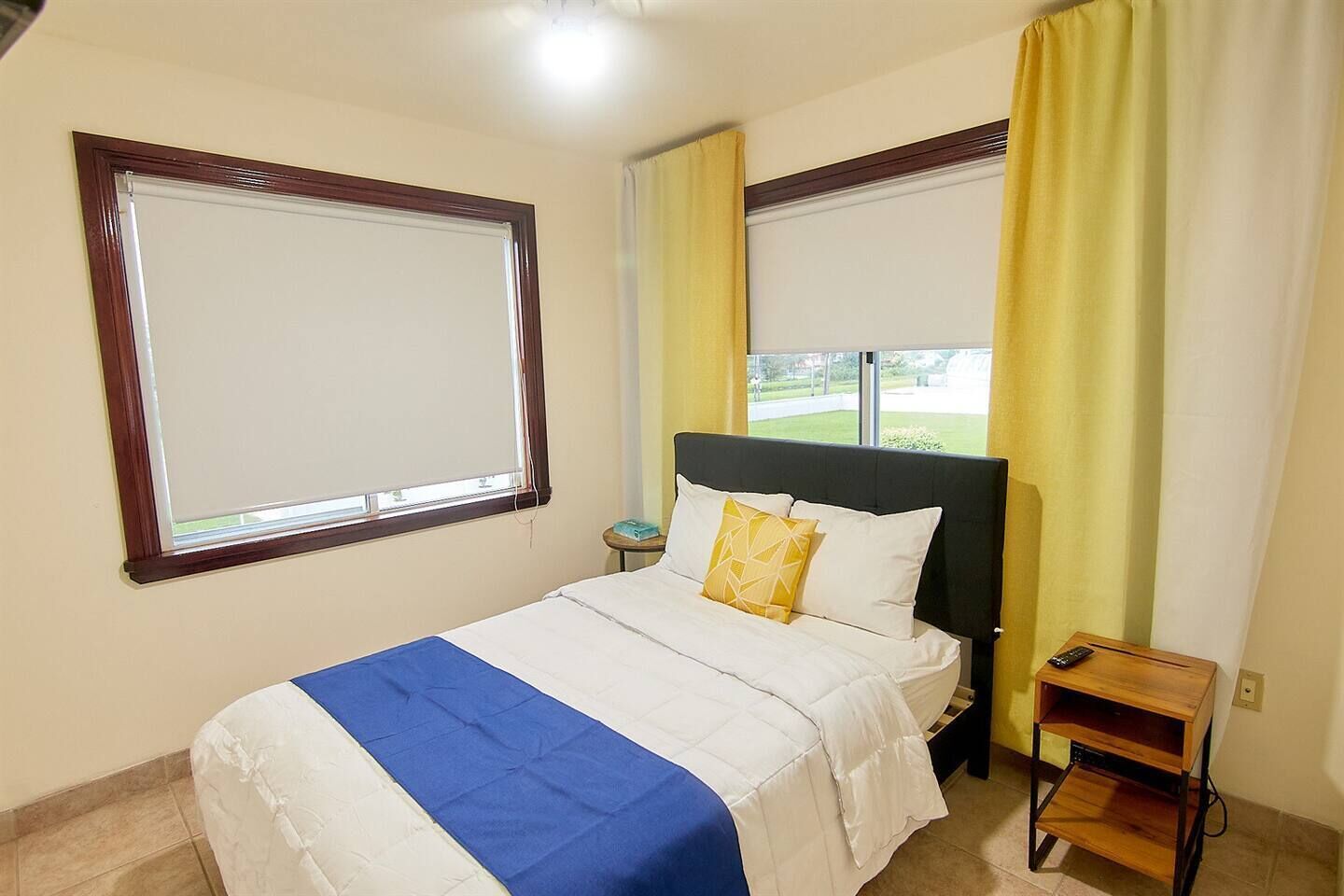 A hotel room with a bed, a nightstand, a window, and curtains.