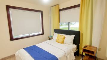 A hotel room with a bed, a nightstand, a window, and curtains.