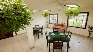 A dining area with a table set for four, surrounded by chairs. There are hanging plants above the table and a window with a view of the outdoors. - Entire Accommodation Suites - Republic Terrace Accommodations (Republic Park, East Bank)