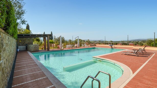 En rektangulär swimmingpool med ett kaklat poolområde, omgiven av solstolar och en pergola.