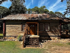 A rustic log cabin with a wooden staircase leading to a front door, surrounded by a stone foundation and a grassy yard. - Peaceful cabin stay with easy access to FIFA matches in Atlanta (Stone Mountain)