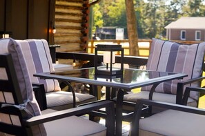 A cozy outdoor seating area with cushioned chairs and a glass-top table, surrounded by a wooden deck and trees. - Rustic Southern Cabin Near Stone Mountain Park • Cozy & Peaceful (Stone Mountain)