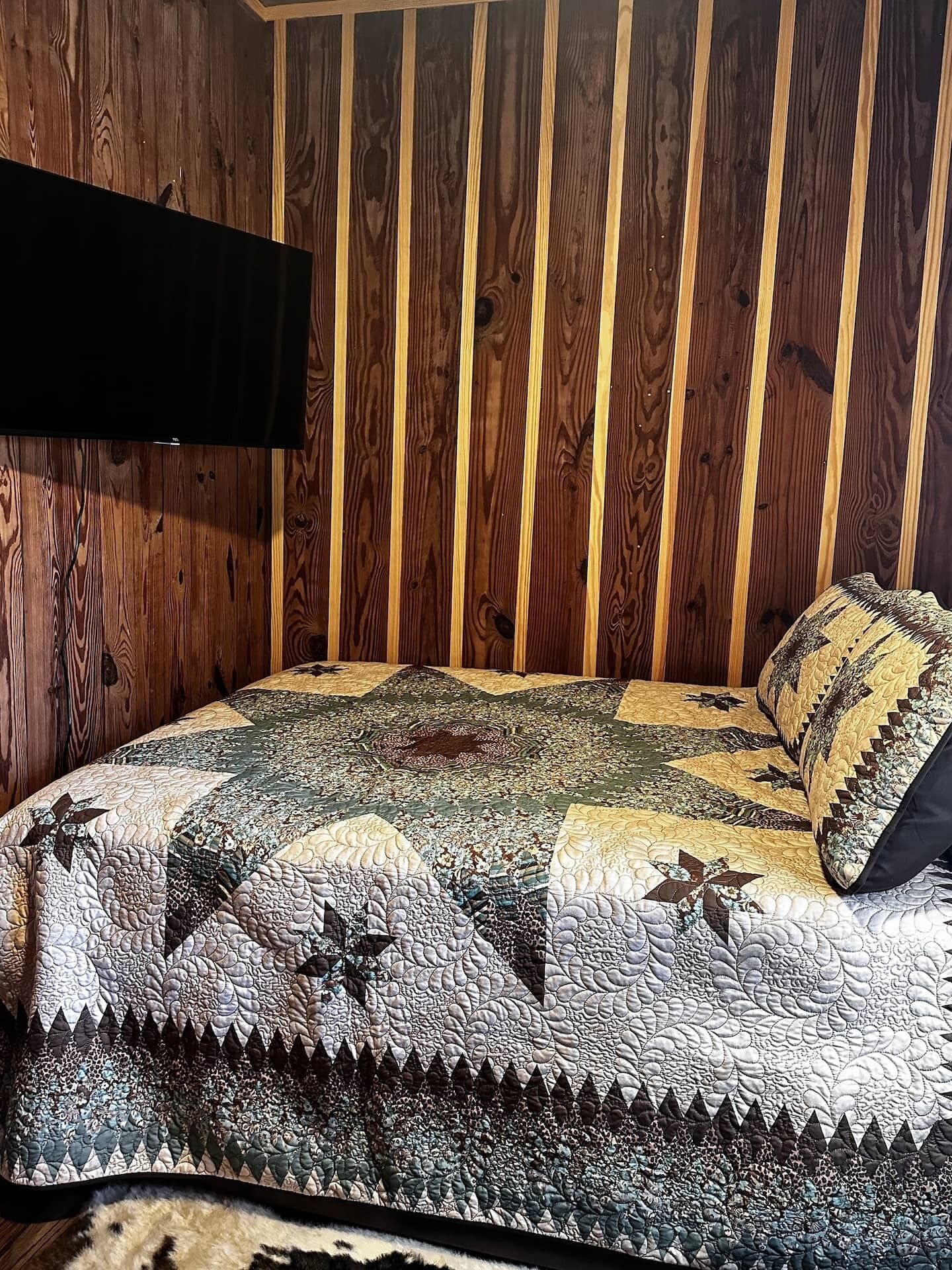 A bedroom with a wooden slat wall, a quilted bedspread, and a mounted television.