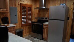 A kitchen with wooden walls, a stainless steel refrigerator, a stove, and a window with blinds. - Rustic Southern Cabin Near Stone Mountain Park • Cozy & Peaceful (Stone Mountain)