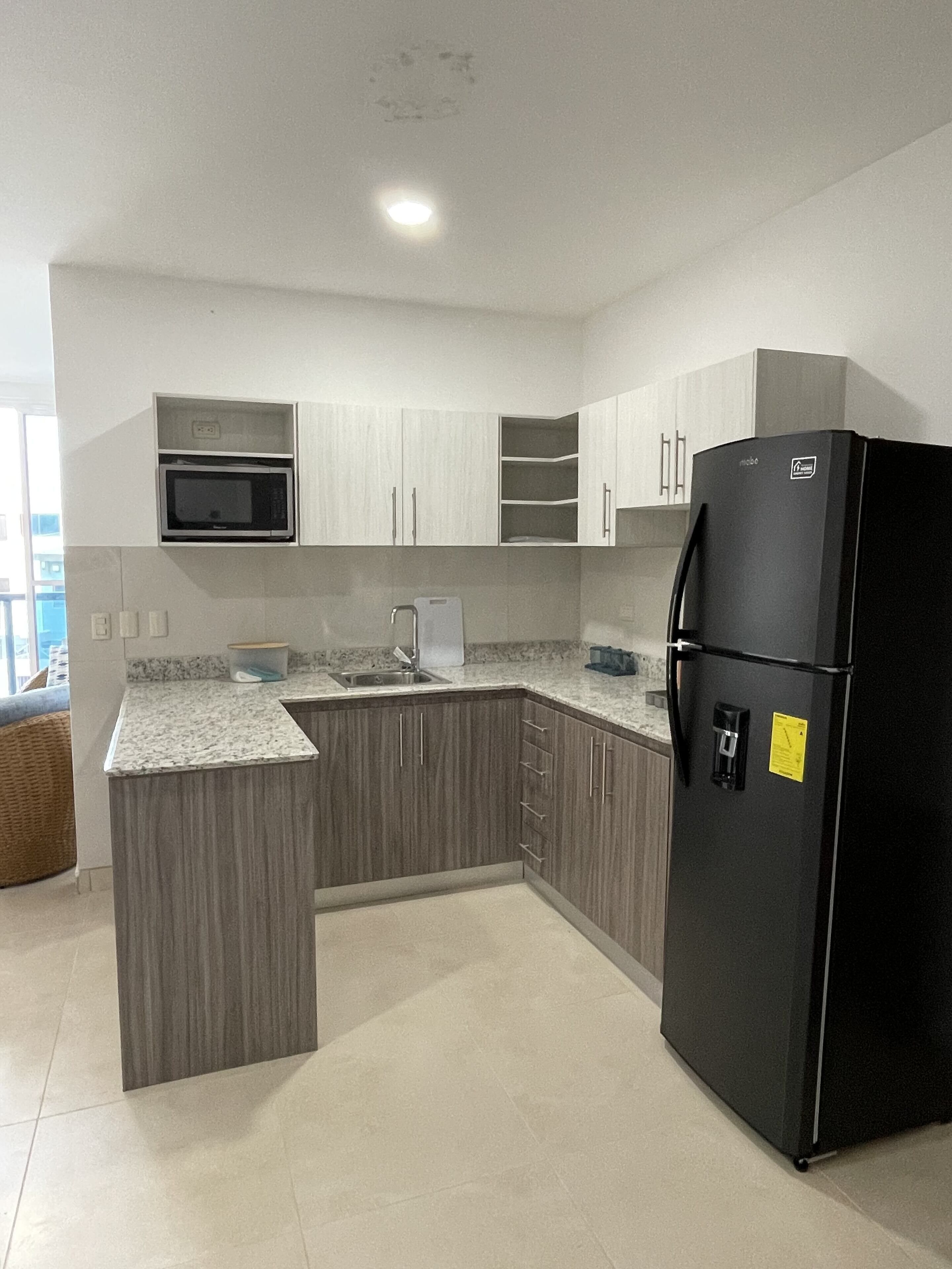 A modern kitchen with grey cabinets, a black refrigerator, and a microwave.