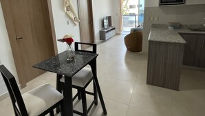 Une cuisine moderne équipée d’un four à micro-ondes encastré, un coin repas avec une table en marbre et des chaises noires, et une vue sur l’extérieur grâce à une grande porte coulissante.