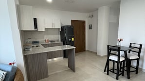 Une cuisine moderne avec un îlot central, un coin repas avec deux chaises et une porte en bois à l’arrière-plan.