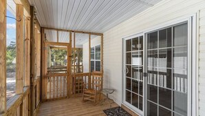 A covered porch with wooden railings, a chair, and a large sliding glass door. - 5min to Attractions, Shops & Beach and Yard Games (Oak Island)