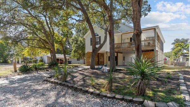 A two-story house with a covered porch, surrounded by trees and gravel landscaping. - 5min to Attractions, Shops & Beach and Yard Games (Oak Island)