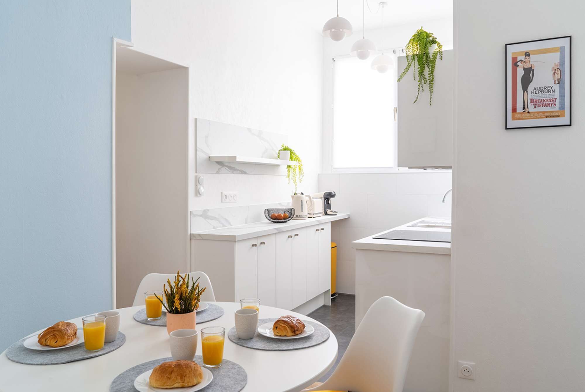 Een moderne keuken met witte kasten, een marmeren spatwand, en een ontbijt klaar gezet ronde eettafel.