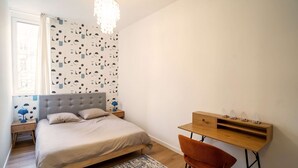 Ein Schlafzimmer mit Bett, Nachttisch, Lampe und Schreibtisch mit Stuhl.