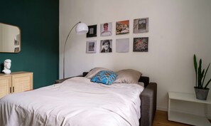 Ein Schlafzimmer mit einem Bett, einem Nachttisch, einer Lampe, einem Spiegel und einer Wand mit gerahmten Bildern.