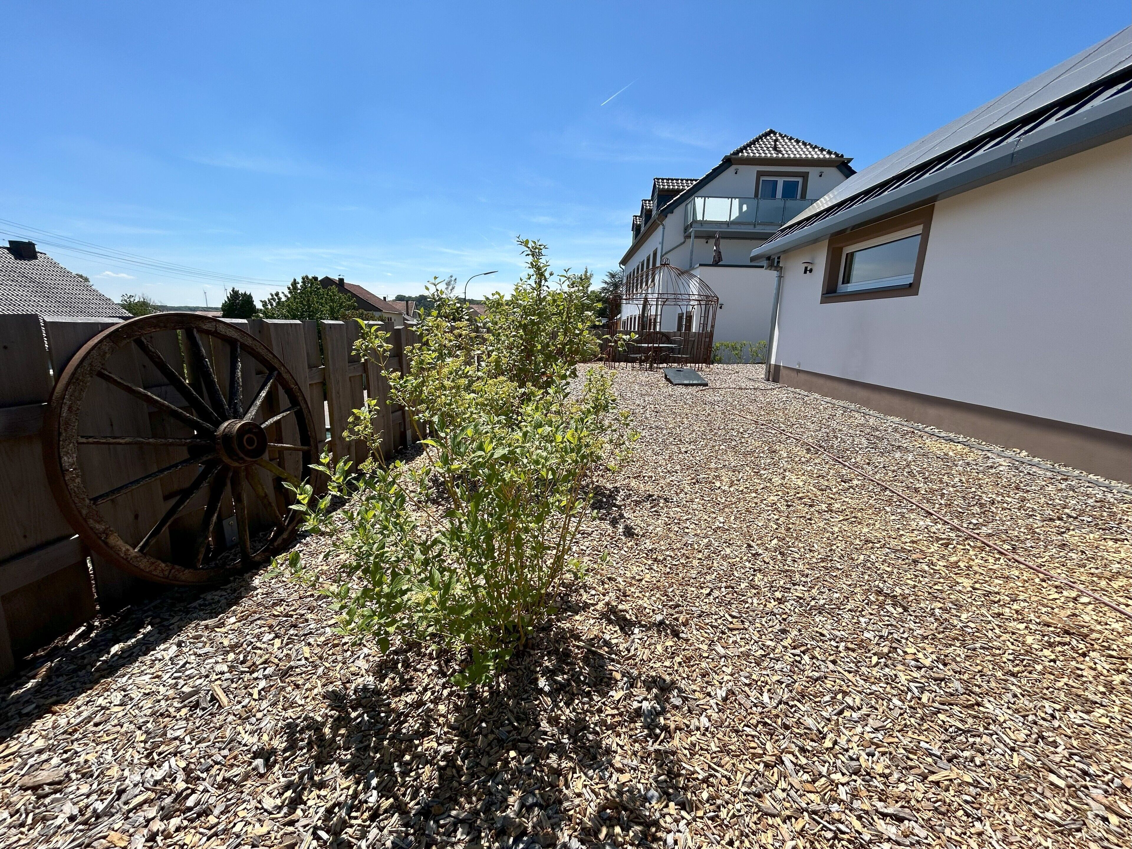 Un quartier résidentiel délimité par une clôture en bois, une porte en métal et un petit jardin agrémenté de gravier et de plantes.