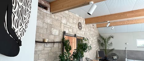 An indoor patio area with a stone wall, wooden beams, a hanging plant, and seating furniture.