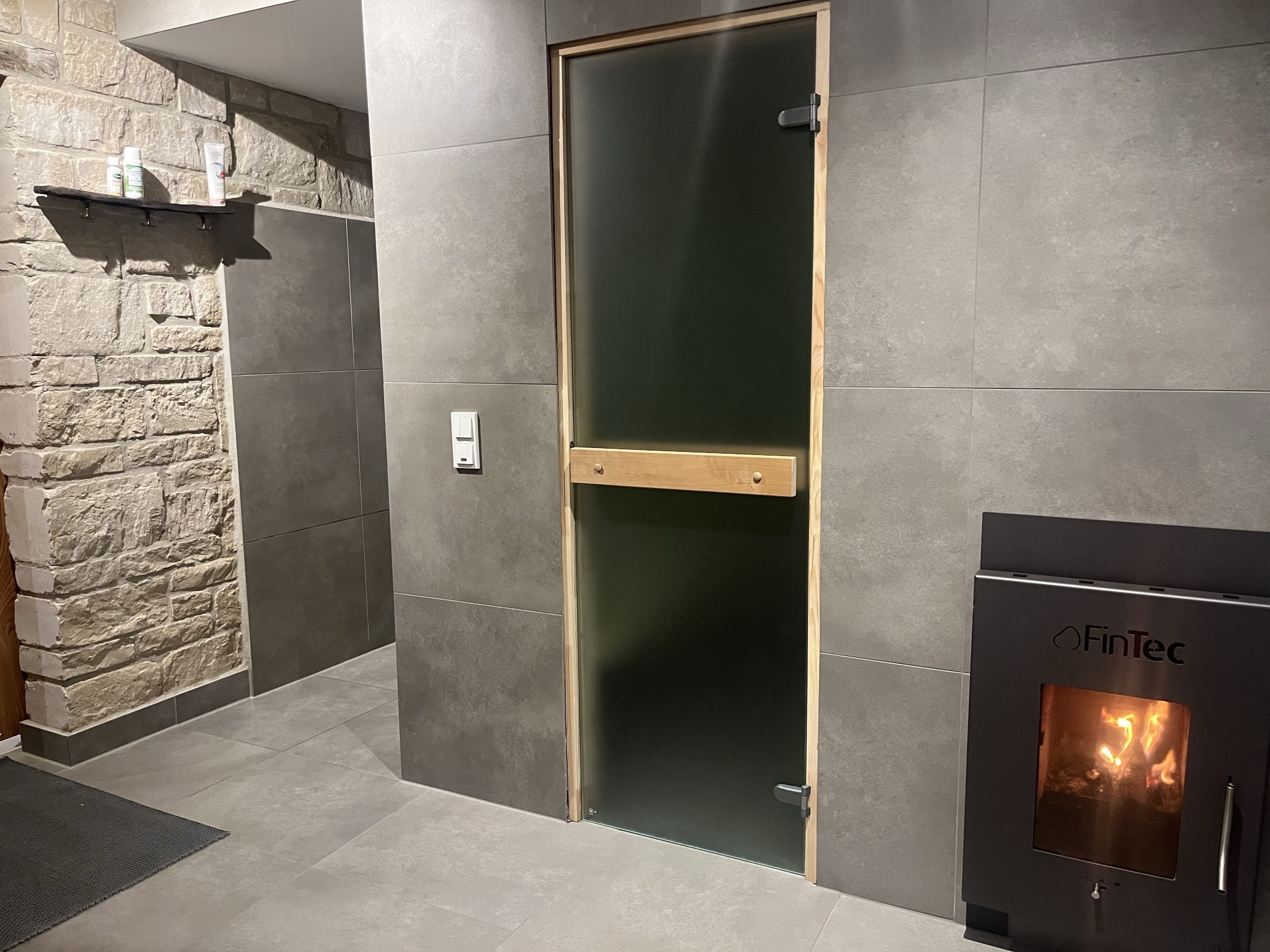 A modern interior with a stone wall, a wooden door, and a fireplace with a visible fire.
