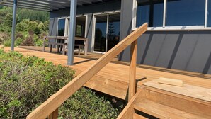 Une maison moderne dotée d’une terrasse en bois, de grandes fenêtres et d’un patio couvert.