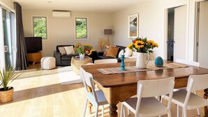 Un vaste espace de vie comprenant une table à manger en bois, des chaises blanches, un canapé noir et un téléviseur.