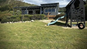 Une maison moderne dotée d’une grande terrasse, d’un toboggan et d’une cabane à jeux.