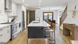 Une cuisine moderne avec des meubles blancs, des appareils en acier inoxydable, un îlot central et un escalier en bois.