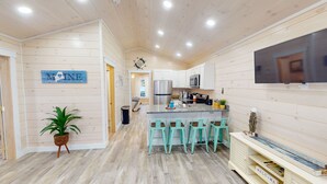 Una cucina moderna con pareti in legno, un'isola centrale con sgabelli da bar, un frigorifero in acciaio inossidabile e una TV a schermo piatto montata a parete.