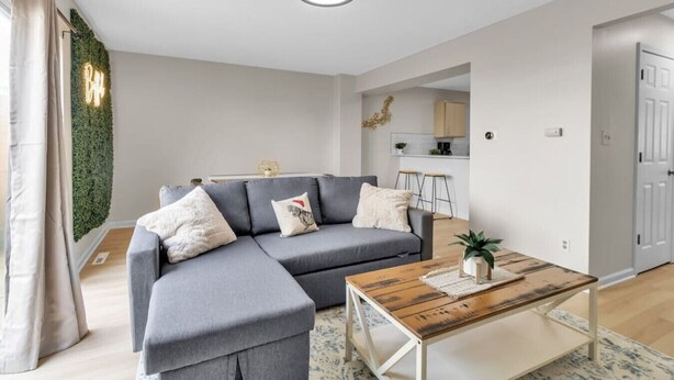 Ein modernes Wohnzimmer mit einem grauen Ecksofa, einem Holztisch und einer Küche im Hintergrund.