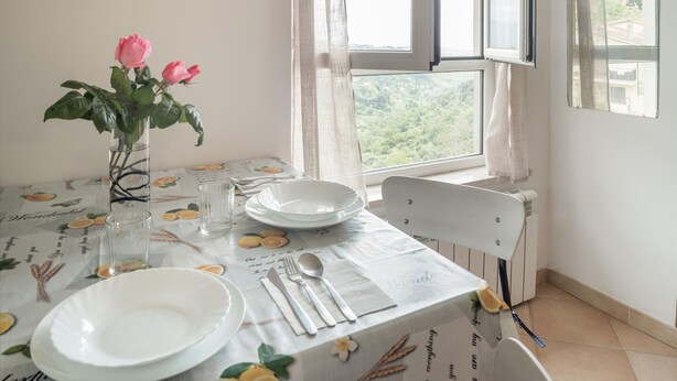 Une table à manger recouverte d’une nappe blanche, avec des assiettes, des couverts et un vase rempli de fleurs roses.