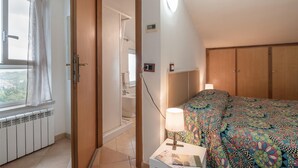 Une chambre à coucher comprenant un lit, une table de chevet avec une lampe, une fenêtre avec des rideaux, un radiateur et une armoire.