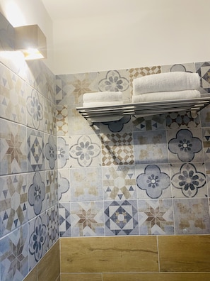 Bathroom features a geometric patterned wall, a metal towel rack, and large, rectangular tiles.