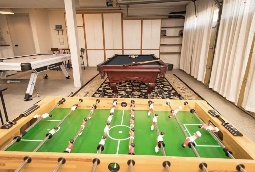 A room with a foosball table, a pool table, and a billiards table.