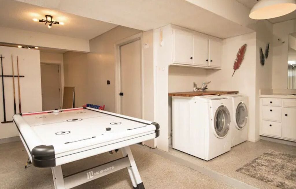 A compact room with a foosball table, a washing machine, and a small kitchenette.