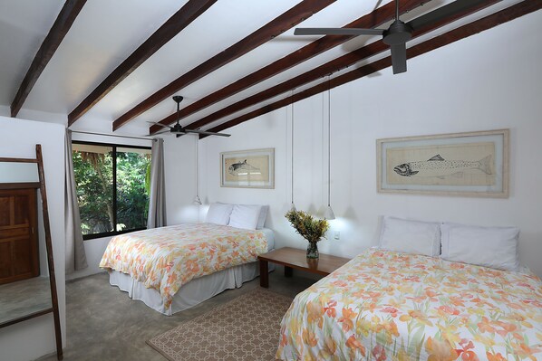 A bedroom with two beds, wooden beams, a ceiling fan, and framed fish artwork on the walls.
