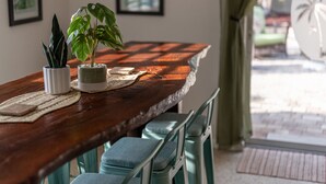 Ein Holztisch mit zwei Blumentöpfen, einer gewebten Tischmatte und einem gerahmten Bild an der Wand.