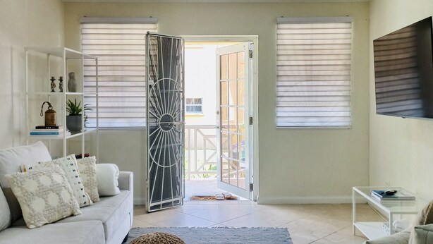 A modern living room with a sofa, ottoman, and coffee table. There is a door leading to an outdoor area. - Idyllic serene secure condo minutes from beach & amenities.  (Bridgetown)