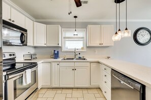 Una cocina con armarios blancos, un horno de acero inoxidable, un lavavajillas, un fregadero y un reloj en la pared.