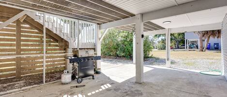 A covered outdoor area with a barbecue grill, concrete floor, and wooden beams.