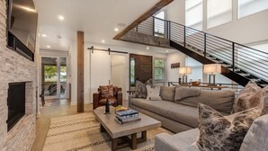 A spacious living area with a fireplace, a staircase, and a large window. - Abode at Sugar Magnolia, outdoor living, private hot tub, Jackson (Jackson)