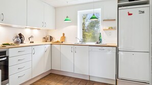 Una cocina moderna con armarios blancos, un refrigerador Bosch y un ventanal con vistas a árboles.