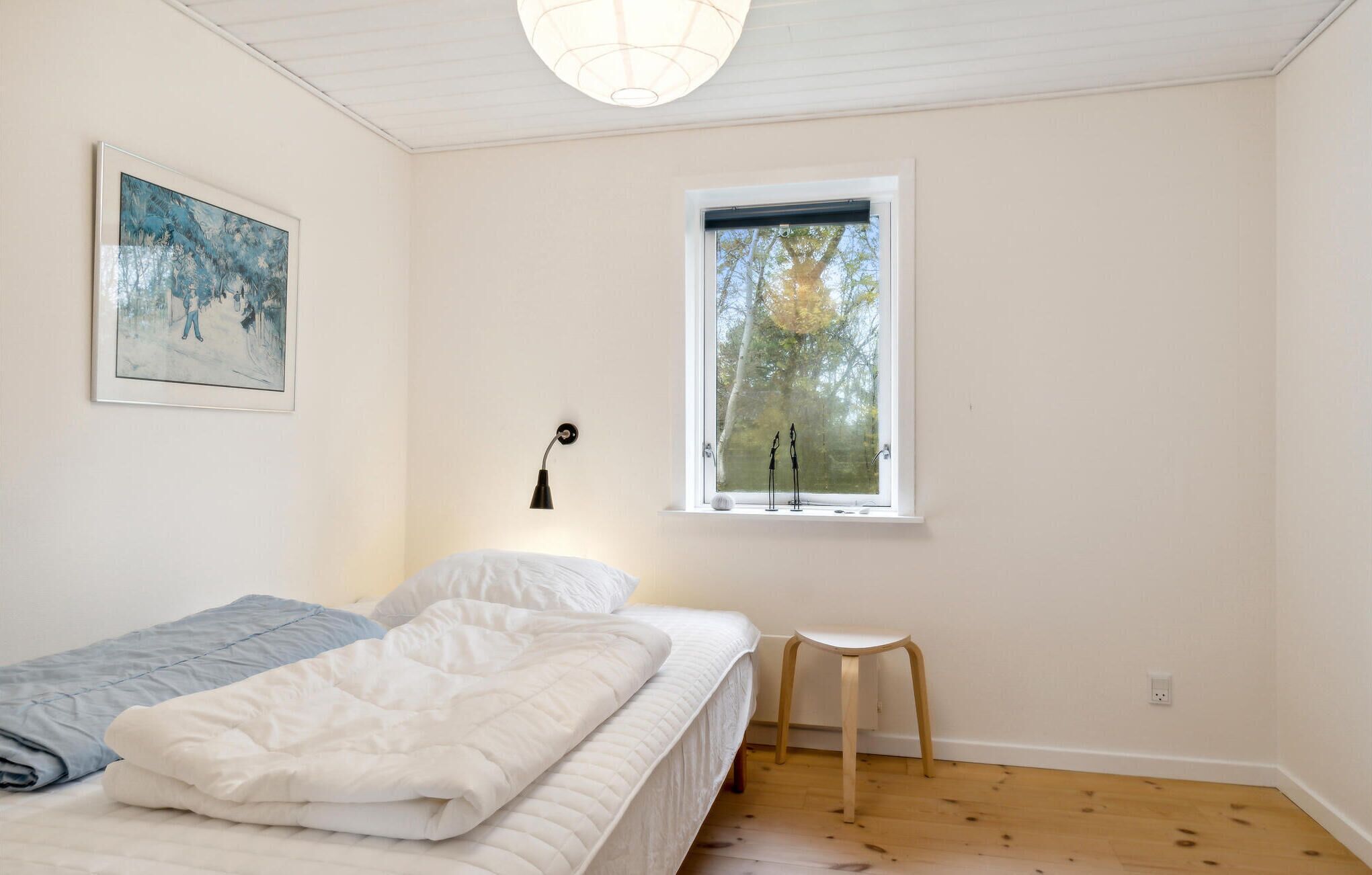 Quarto com cama, janela com vista para árvores, um quadro na parede e abajur.